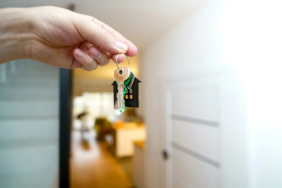 Hand hält einen Hausschlüssel mit Anhänger in Hausform